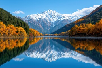 Fototapeta premium Majestic mountains reflecting in a calm lake surrounded by colorful autumn trees and clear blue skies.