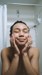 Naklejka premium Person smiling while washing face, standing in bathroom setting