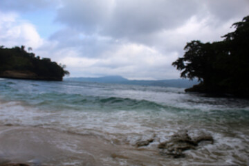 Blur view of white sand beach in summer with sea water and waves washing the shore.