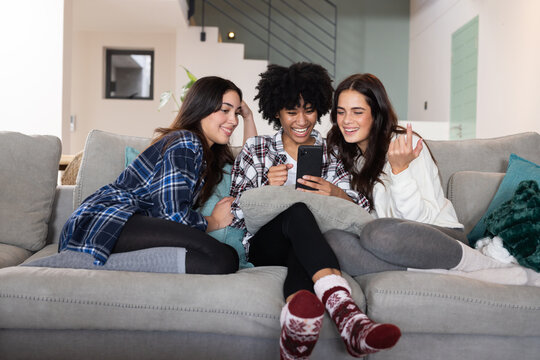 Christmas time, mutliracial female friends on couch laughing and looking at smartphone, at home