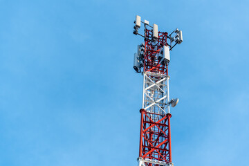 Close-up of a red and white telecommunications tower against a clear blue sky, displaying modern wireless equipment for high-speed data transmission. High quality photo