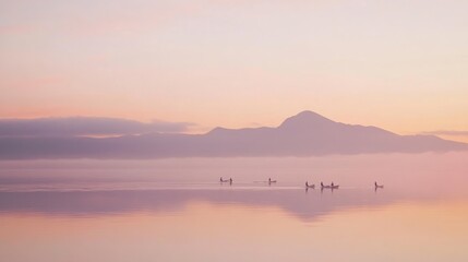 Fototapeta premium A group of birds silhouetted against a misty mountain range during a colorful sunset.
