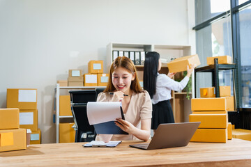 Two young female entrepreneurs work together in warehouse with parcel boxes, wooden tables, and shelves. prepare sales brochures, social media templates, business proposals for small online business.