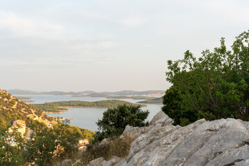 Stunning view of rocky hillside with lush green foliage and a serene coastal landscape in the background at sunset. Concept of nature exploration, peaceful seaside scenery, and Mediterranean beauty.