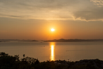 Obraz premium Stunning sunset over calm sea with golden reflections on the water and silhouetted islands in the distance. Travel, relaxation, and scenic photography. High quality photo