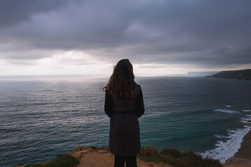Mujer joven que se siente sola y triste  o pensativa o esperando. mirando el mar en un día sombrío , Young woman feeling alone and sad or thoughtful or waiting. looking at the sea on a gloomy day