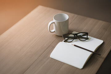 Notebook, pencil, glasses, coffee cup on wooden table. Morning time with sunlight, relaxation concept.