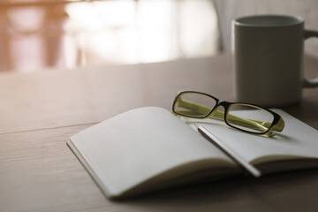 Notebook, pencil, glasses, coffee cup on wooden table. Morning time with sunlight, relaxation...