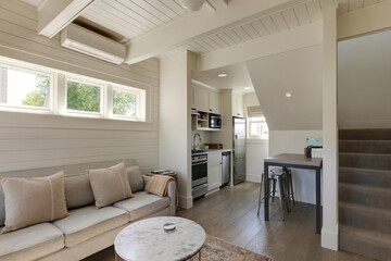 This traditional cottage interior features a compact, efficient kitchen with white cabinetry, stainless steel appliances, and a cozy dining nook with bar stools under the staircase.