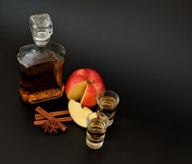Apple liqueur with cinnamon and anise on a black background, in a bottle and two glasses with...