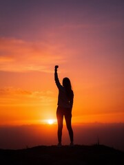 Fototapeta premium Empowered Silhouette of a Woman Raising Fist Against Sunset Background