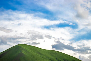Green hill under a bright blue sky with white clouds, perfect for copy space.