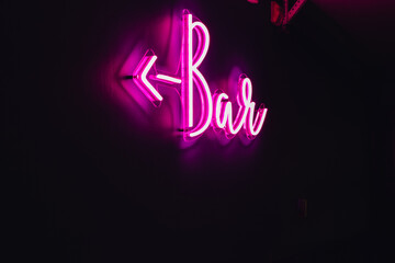 glowing pink neon Bar sign with arrow on a black background