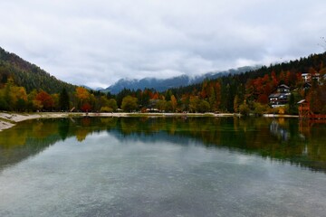 Fototapeta premium Shore of lake Jasna near Kranjska Gora in Gorenjska, Slovenia with a reflection in the water and yellow and red trees,