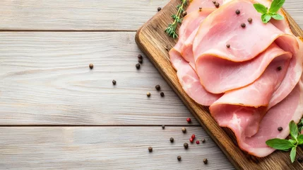 Thinly sliced ham on a wooden cutting board with herbs and peppercorns. © Thamonchanok
