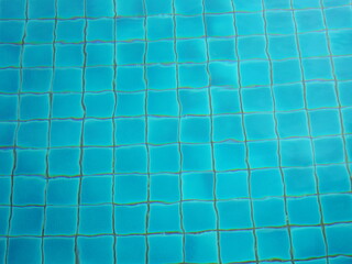 The rippling water in the pool gives the floor wavy appearance. Ripple water in blue pool. The pool is tiled with blue ceramic tiles. Blue water serface. Blue ocean rippled water texture reflection

