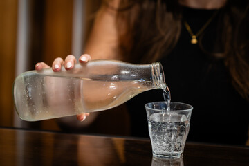 Pouring water into a glass at a cafe. Premium filtered water at a restaurant. Sparkling or still water, soda, mineral water or hydration options drinking from a glass. Close up view.