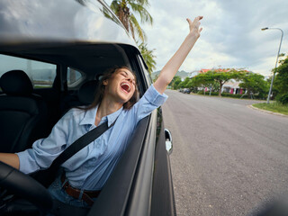 Woman in car smiling, arms raised in joy a woman is seated in the driver's seat of a car with her...