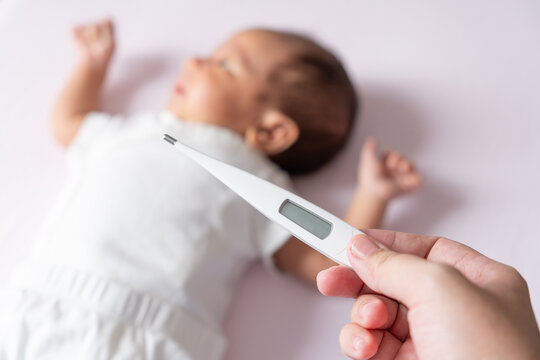 A mother gently checks her baby temperature with a thermometer, ensuring her little one is comfortable and healthy, with tender care and concern.