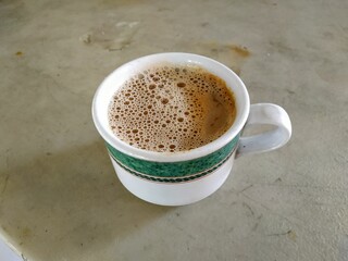 A cup of frothy coffee in a white mug with a green decorative band, placed on a textured surface.
