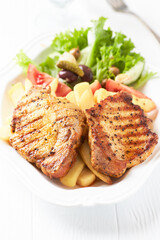 Grilled Steaks with french fries and fresh salad. Bright wooden background.