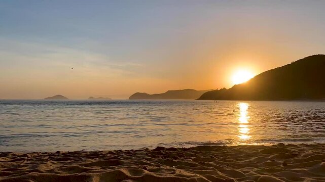 Time-lapse p&ocirc;r do sol na praia movimentada. Muitas pessoas caminhando, nadando e praticando esportes e ao fundo, no mar, alguns barcos passando e tamb&eacute;m, quatro ilhas famosas do litoral norte.
