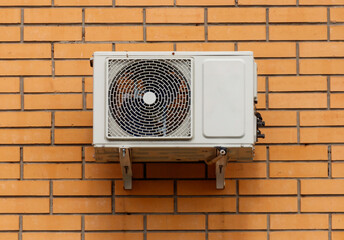 A white air conditioner unit is mounted on a brick wall