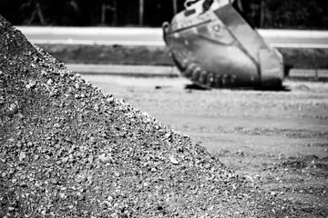 Aggregate dirt pile at a construction site with a defocused excavator bucket in the background.