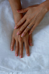 One Hand with a Ring Resting over the other one on a White Blanket