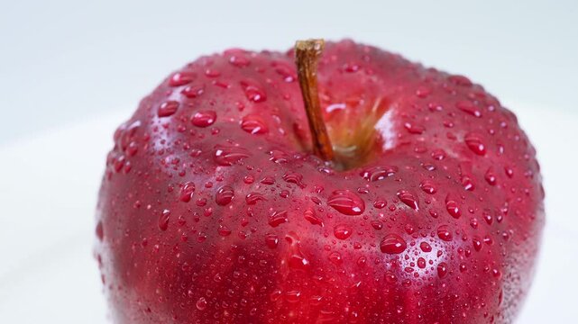 Red apple with water droplets on a white table, close-up