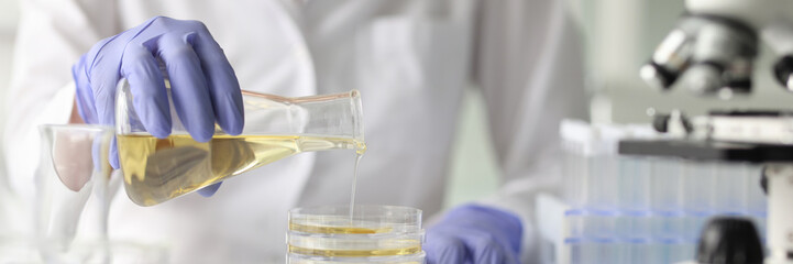 Assistant pours yellow liquid from flask at desk in lab