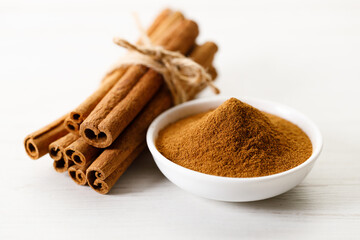 Dried Cinnamomum cassia and cinnamon powder on white wooden table.