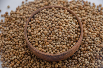 Fototapeta premium Coriander seeds in a wooden plate on a white background