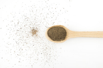 black ground pepper in a wooden spoon on a white background
