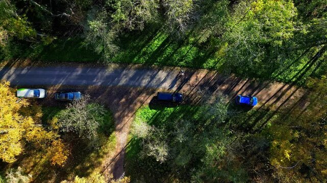 Drone tops down cars parket in green countryside forest dusty road with people walk