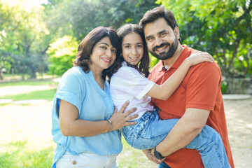 Fototapeta premium Young happy indian family enjoying in summer park or garden. father carrying, holding her daughter on shoulder. holiday or vacation. Parents with child daughter bonding, love and care.Togetherness.