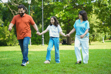 Happy indian family holding hands walking in summer park, Playful parents with child daughter...