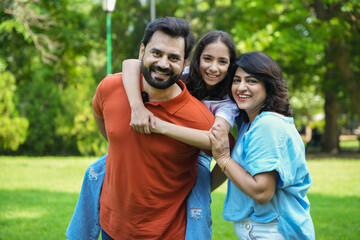 young Indian father carrying, piggyback his daughter in the park. family of three enjoying vacation...