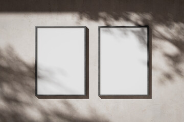 Two blank white portrait A0 posters in a metal frame on a plaster wall © Yevhen