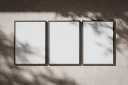 Three blank white portrait A0 posters in a metal frame on a plaster wall