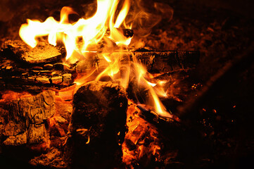 A close-up shot of a burning log in a campfire. The flames are dancing and the embers are glowing