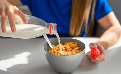 Dziewczynka jedząca śniadanie płatki kukurydziane ze świeżym mlekiem, wlewa mleko z butelki do miski © Paweł Kacperek