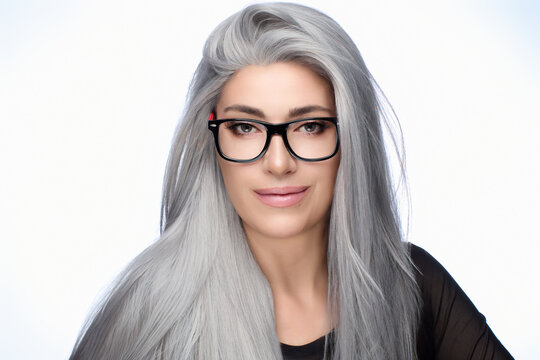 Confident woman with long gray hair wearing stylish glasses, smiling against a white background, showcasing eyewear fashion and elegance