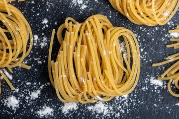 Bundles of uncooked spaghetti are artistically arranged on a textured black slate surface, lightly...