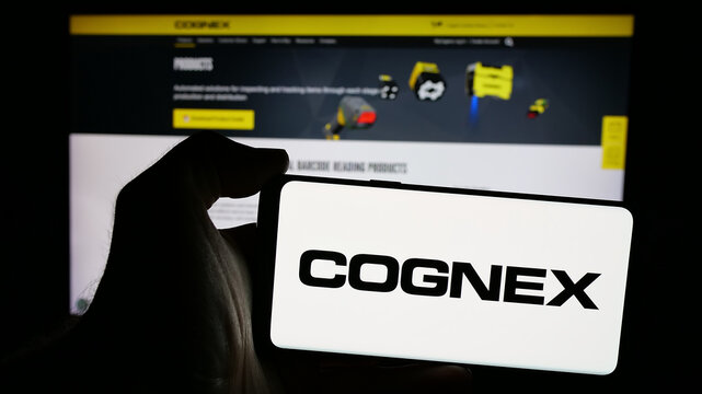 Stuttgart, Germany - 10-18-2024: Person holding smartphone with logo of US machine vision company Cognex Corporation on screen in front of website. Focus on phone display.