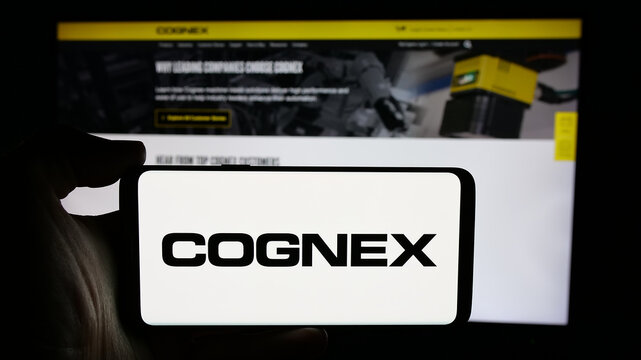 Stuttgart, Germany - 10-18-2024: Person holding cellphone with logo of US machine vision company Cognex Corporation on screen in front of webpage. Focus on phone display.