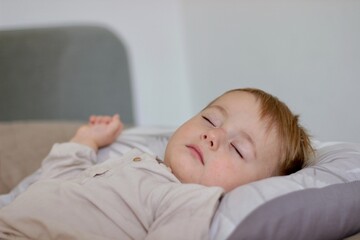 During the day, the child sleeps. The baby is daydreaming, he is lying on a light bed in a beige shirt