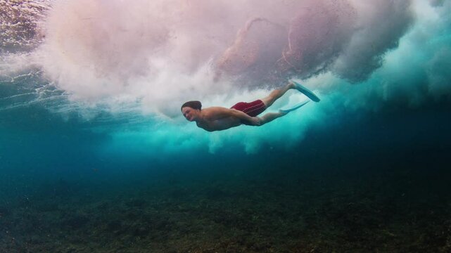 Young man swims in the ocean with waves. Man dives underwater under the breaking ocean wave on sunrise. Person swims in the crushing waves