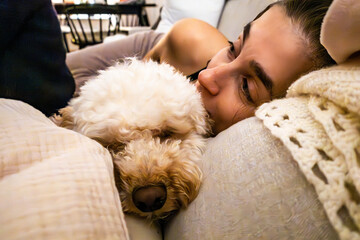 A 30-year-old woman relaxes on the couch with her Bichpoo poodle dog.