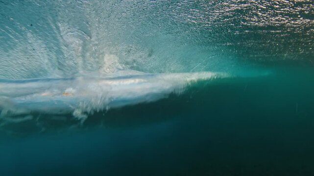 Young man swims in the ocean with waves. Man dives underwater under the breaking ocean wave on sunrise. Person swims in the crushing waves